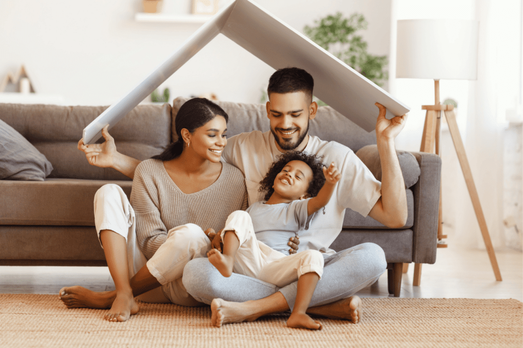 Famille souriante formant un toit symbolique avec un panneau, illustrant la protection offerte par l’assurance emprunteur en cas de risque aggravé de santé selon la convention AERAS.
