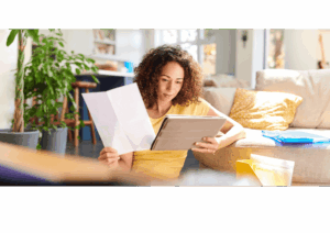 Femme gérant ses finances personnelles à la maison, consultant des documents et une tablette, illustrant le processus de réflexion avant un rachat de crédit.
