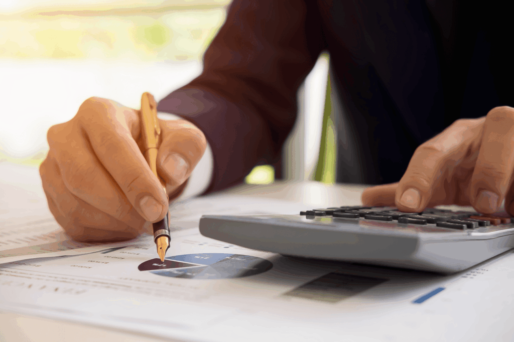 Une personne utilisant une calculatrice et un stylo pour analyser des documents financiers avec des graphiques, illustrant des calculs liés au factoring ou affacturage