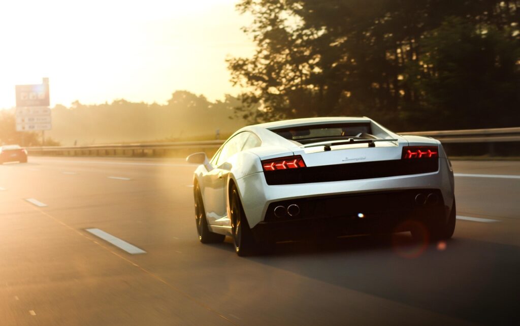 Cette image capture une scène dynamique mettant en vedette une Lamborghini Gallardo LP 560-4 blanche filant sur une autoroute baignée par la lumière dorée du soleil couchant.