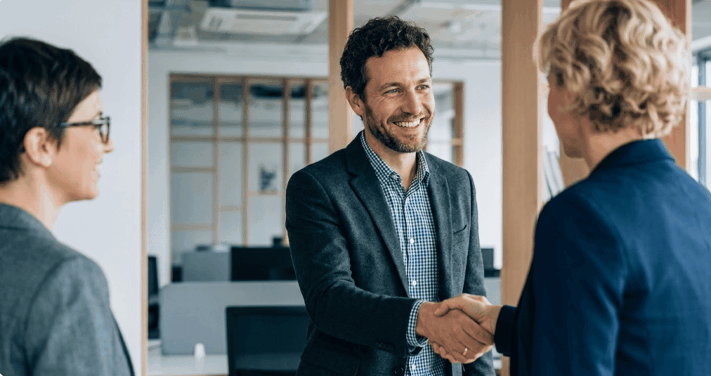 Un homme dirigeant et une femme conseiller financier se serrent la main dans un bureau, suite à la conclusion d'un obo immobilier