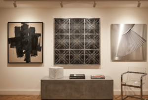 Photographie d'une collection d'art, présentant une sculpture murale géométrique d'OP-Art, une peinture abstraite en noir et blanc de grand format et une photographie conceptuelle en métal poli.